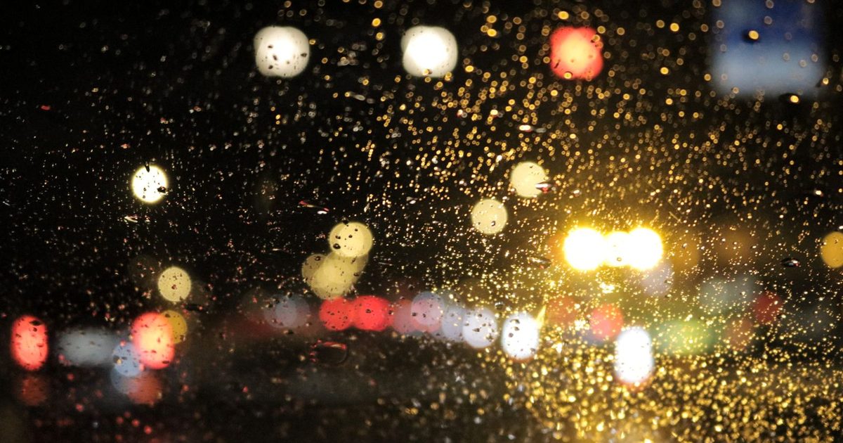 Street lights through raindrops on a car window at night